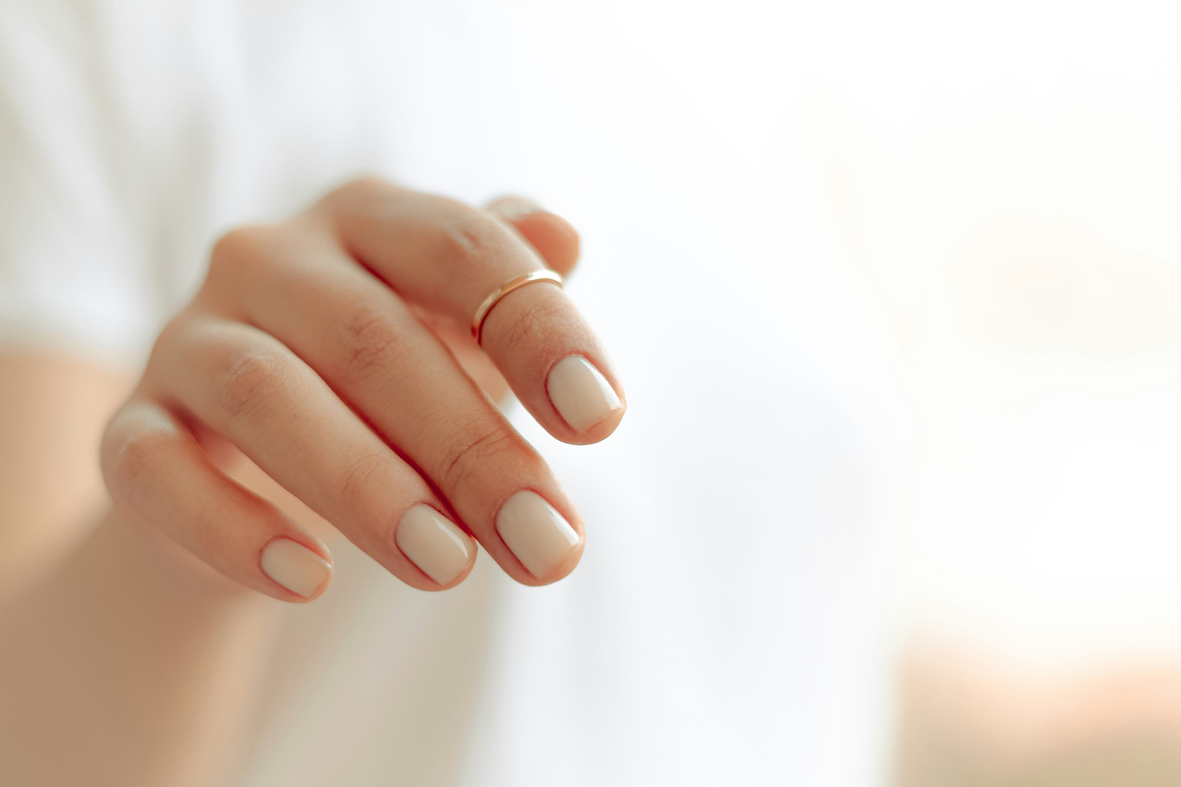 A hand with a glossy soft-white gel manicure against a near-white background